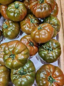 A crate filled with green and brown heirloom tomatoes, featuring the unique Tomato 'Black Russian' 4" Pot, enhances the rustic charm of the display.