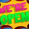 A colorful sign with an "WE'RE OPEN!!!!" announcement features a person in a pink tutu holding a star wand, set against a vibrant backdrop.