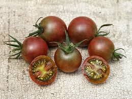 Five dark red 'Black Cherry' tomatoes, with two cut in half, are elegantly displayed on a textured surface.