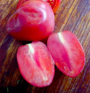 Two halved Tomato 'Mamma Mia' alongside a whole one on a wooden surface evoke the simple joys of an Italian cooking session.