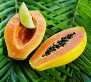 A Paw Paw 'Fijian' papaya, halved with seeds and adorned by a lime wedge, rests gracefully on green palm leaves.
