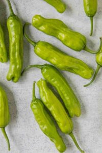 Several Capsicum 'Shishito' chilli peppers are scattered on a light gray surface.