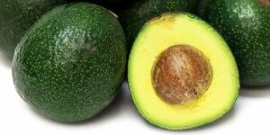 Close-up of whole and halved Persea 'Reed' Avocado 4L Pot revealing the seed and creamy green flesh.
.