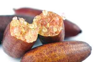 Close-up of sliced Citrus 'Pink Ice' Finger Lime, revealing its pink citrus pearls atop whole fruits against a white background. Perfect for cultivation in a 6" pot.
