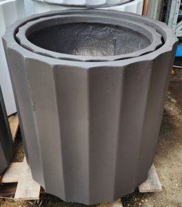 The GardenLite Grecian Cylinder Black S 39x39cm planter, featuring a dark matt finish and vertical ridges, is shown outdoors on a wooden pallet.