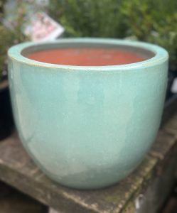 A Glazed Cylinder Moss Green S 20x20cm pot sits on a stone surface, with blurred green foliage in the background.