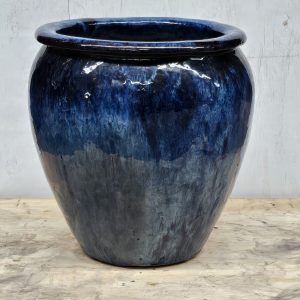 A large, glossy, dark blue ceramic vase with a rounded shape and wide rim, standing on a wooden surface.
