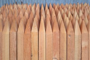A close-up of Garden Stake Timber (25mmx25mmx1500mm) with pointed tops, stacked vertically before a corrugated metal wall—ideal for garden use.