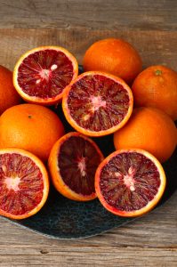 A 4L Citrus ‘Arnold’ Blood Orange sits on a wooden surface, its vibrant red and orange flesh displayed—perfect for refreshing recipes.
