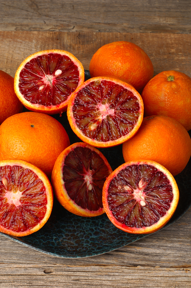A 4L Citrus ‘Arnold’ Blood Orange sits on a wooden surface, its vibrant red and orange flesh displayed—perfect for refreshing recipes.