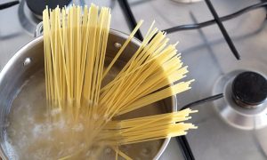 Uncooked spaghetti partially submerged and standing upright in a pot of boiling water on a gas stove—perfect for quick meals before diving into your favorite Garden Hacks.