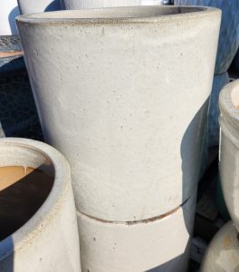 Two large, stacked, off-white ceramic pots with a smooth, slightly speckled surface, shown outdoors in sunlight.