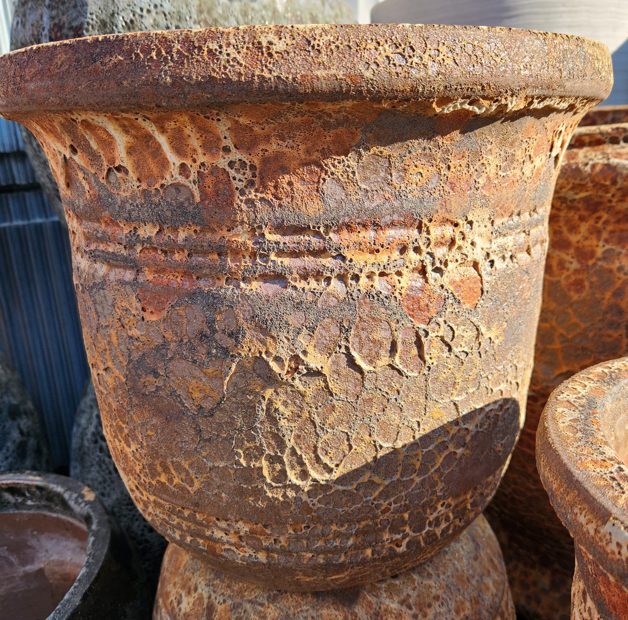A close-up of a large, weathered terracotta planter with a rough, textured surface and decorative horizontal ridges.