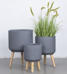 Three white GardenLite Corrugated Cylinder Planters with wooden legs (XS 25x25cm) are displayed; one holds tall, green grass-like plants whilst the other two remain empty—ideal for creating a modern GardenLite style.