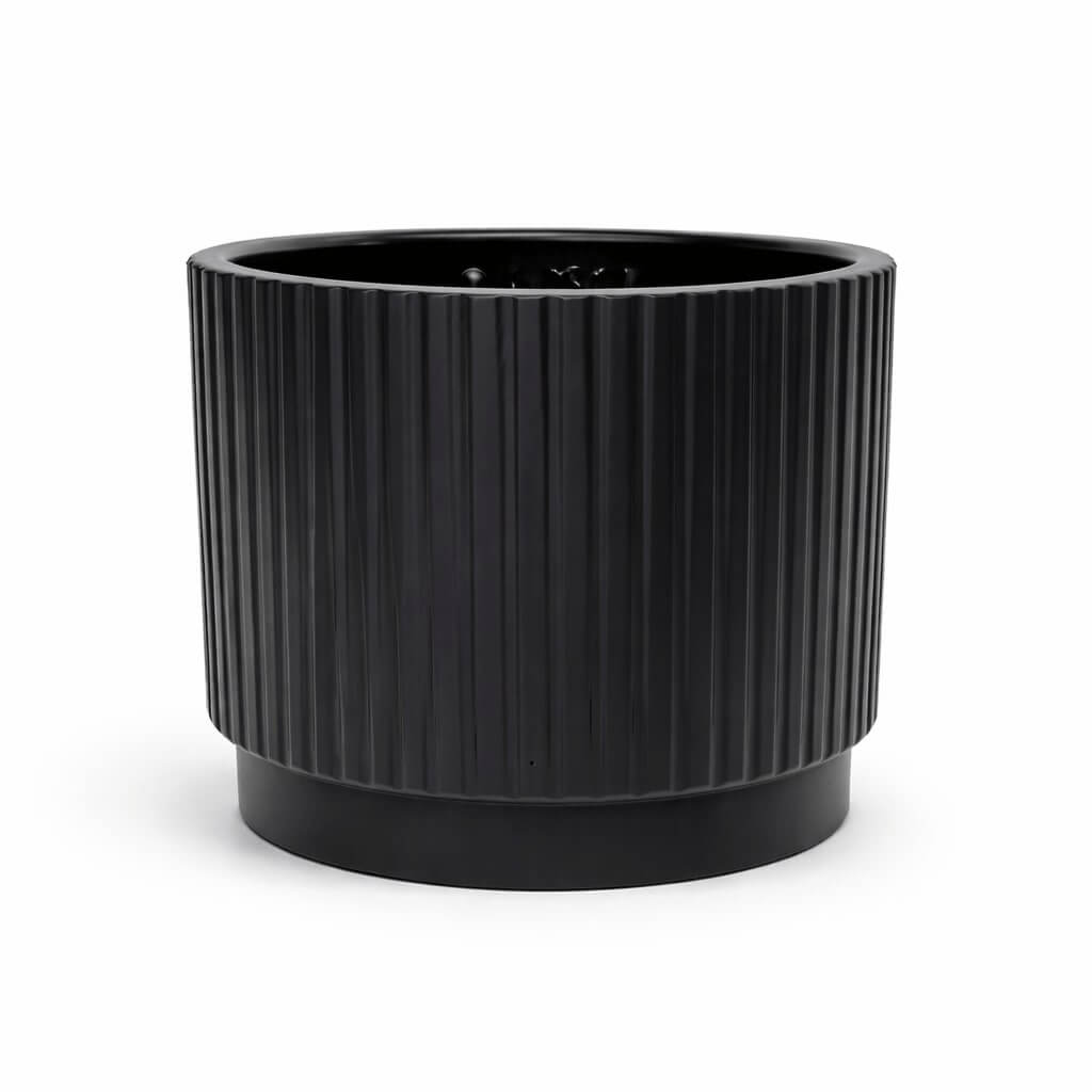 A black, cylindrical planter with vertical grooves sits on a solid base against a white background.