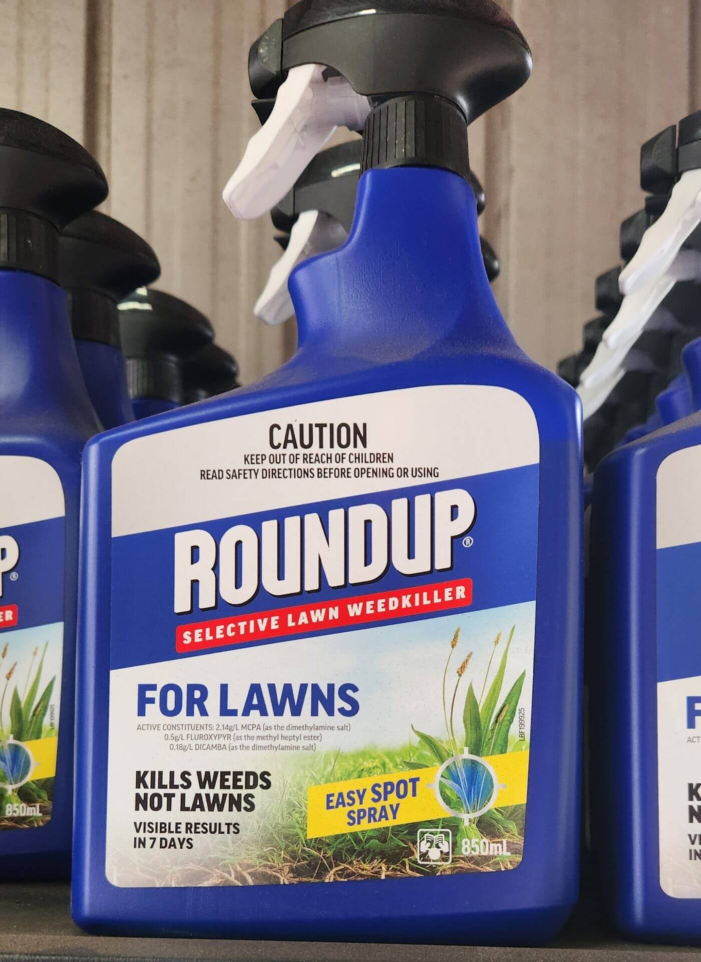 A blue bottle of Roundup Selective Lawn Weedkiller for lawns, labelled as killing weeds but not lawns, with "Easy Spot Spray" and safety caution visible on the packaging.