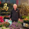 A man stands in front of colourful flowers and plants with gold Chinese zodiac symbols, a horse illustration, and lanterns at the Holiday Plant Sale, celebrating the Year of the Fire Horse 2026.